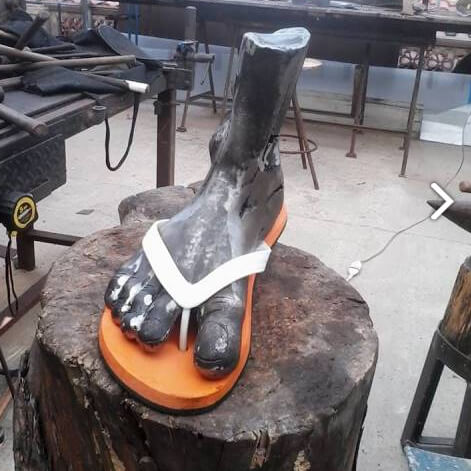 Lucida Follia: an iron cast of a bare foot wearing a white flip-flop, resting on a tree stump in the workshop.