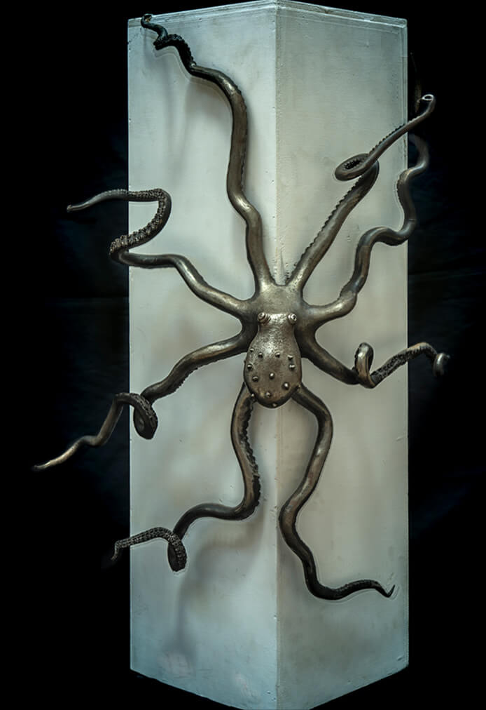 Forged iron octopus clinging to a pale stone plinth, its eight tentacles curling around all four sides.