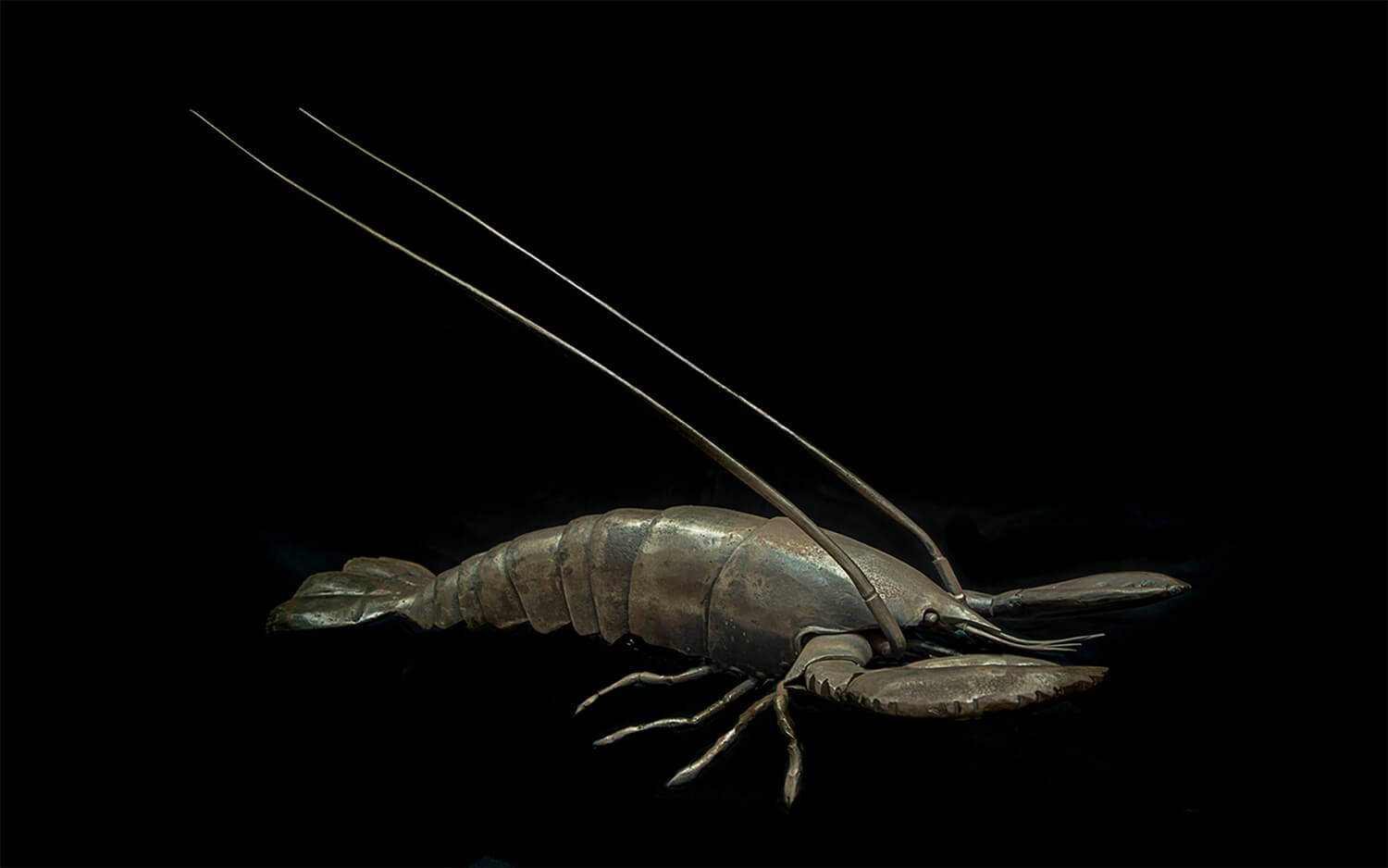 Forged iron lobster with sectioned shell, raised claws and two antennae sweeping the full width of the frame.